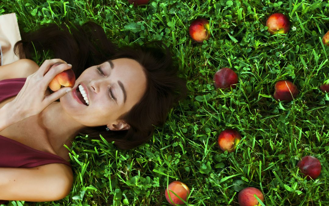 Beautiful happy young woman smiling eating a peach